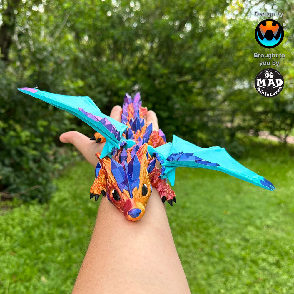 Baby Crystal Wolf Dragon from Mad Miniatures, designed by Cinderwing, perched on a hand with wings spread. The dragon’s shimmering body contrasts beautifully with the turquoise wings.