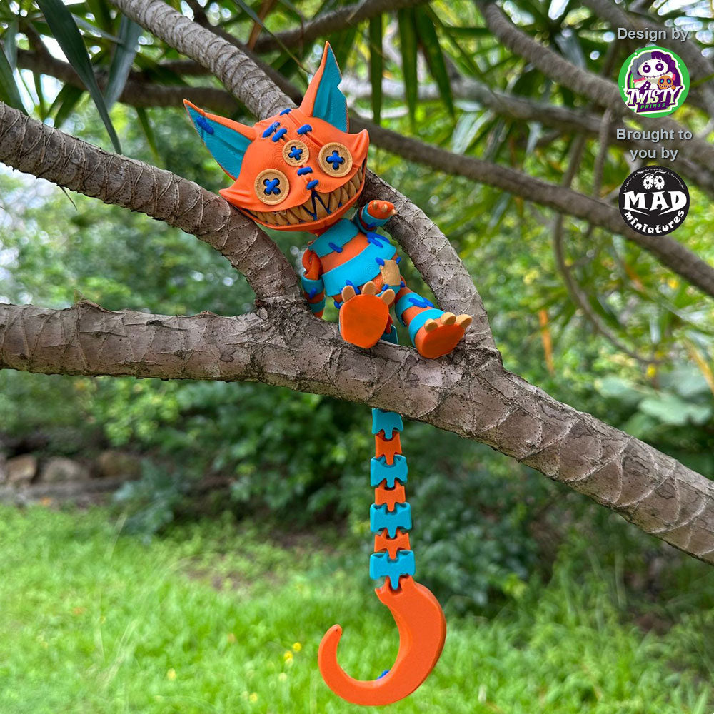Stuffed Cat sitting in a tree, with her long tail hanging down, showcasing her vibrant orange and turquoise patchwork design and quirky stitched features.