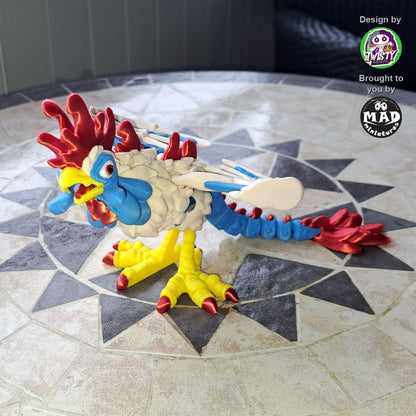 3D-printed articulated Cockatrice by Mad Miniatures in red, yellow, blue and green with detailed wings and claws, posed on a wooden base.
