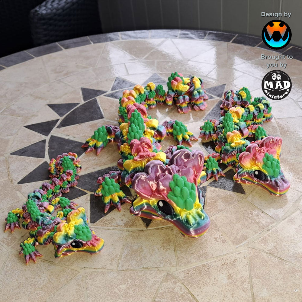 3D-printed articulated Snapdragon Dragon by Mad Miniatures in rainbow colours with plant-green flower accents, inspired by snapdragon plants.