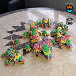 3D-printed articulated Snapdragon Dragon by Mad Miniatures in rainbow colours with plant-green flower accents, inspired by snapdragon plants.
