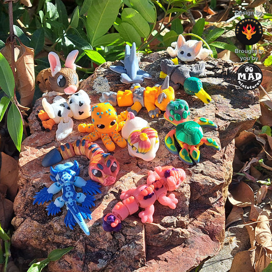Mini Critter Collection – Series One by Mad Miniatures, featuring 12 multicolour 3D-printed mini animals and dragons on a rock in sunlight